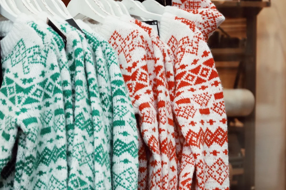Rack of white wool sweaters with green and red Nordic geometric patterns on white hangers