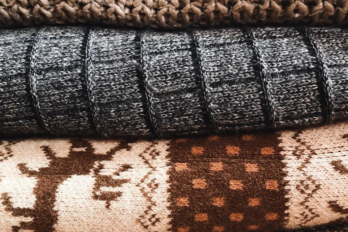 Stack of folded wool knits: a chunky tan knit, a gray ribbed knit, and a brown and cream patterned knit