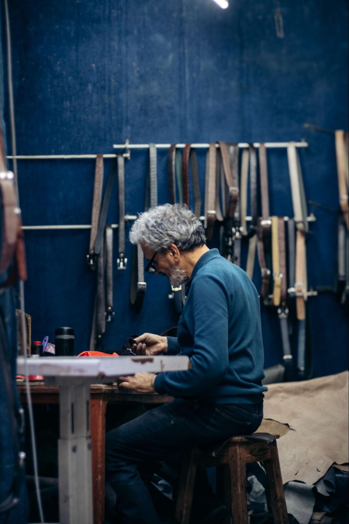 Leather craftsman working by hand in a workshop surrounded by leather straps, representing European artisan slow production