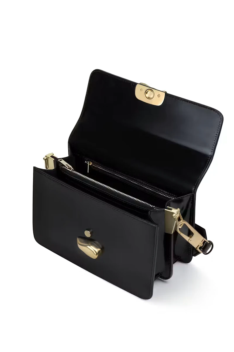 Black CHYLAK shoulder bag with sculptural gold seal, open to show its compartments