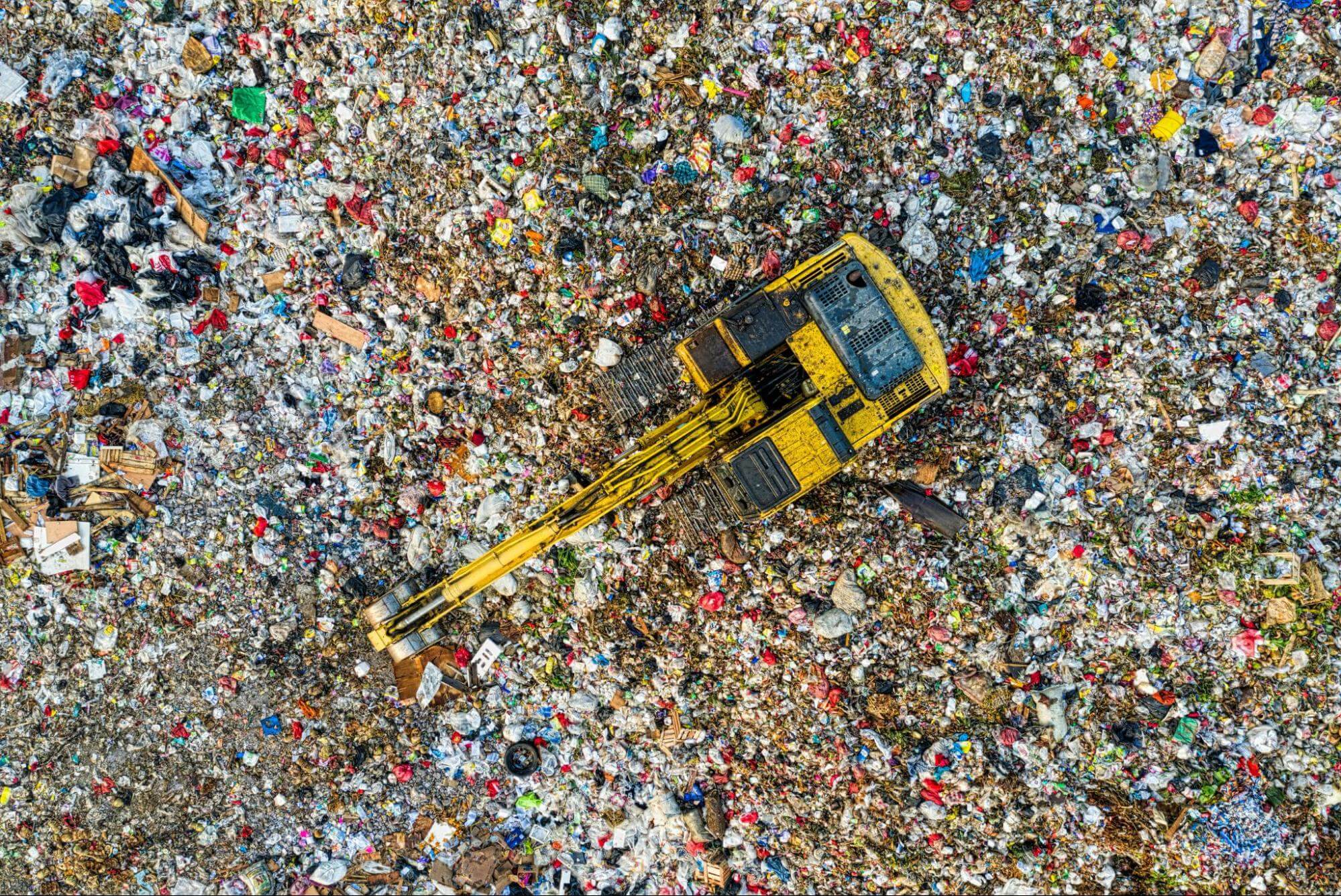 Aerial view of a large landfill site with a yellow bulldozer, illustrating the scale of overconsumption and waste