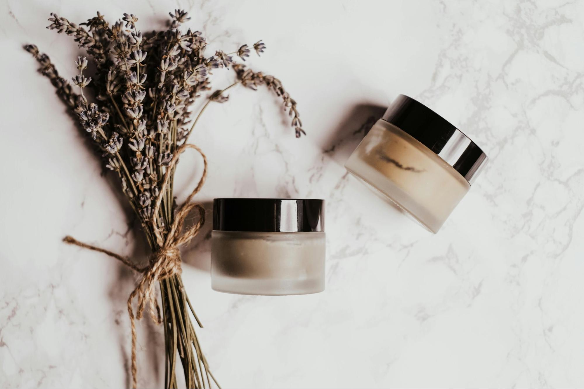 Dried lavender bundle beside elegant glass skincare jars on a marble surface, representing European botanical beauty traditions